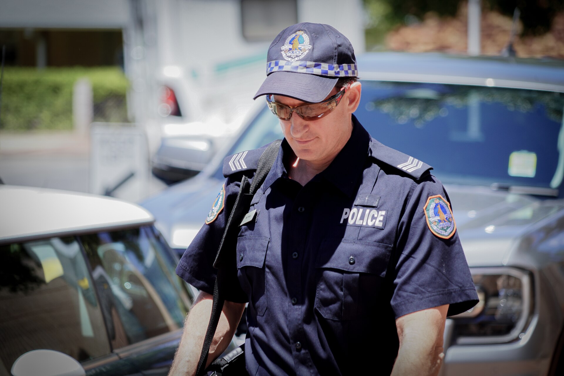 A man in NT Police uniform walking down the street, on a sunny day.