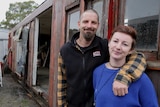 Couple with arms around each other standing in front of old run-down train carriage