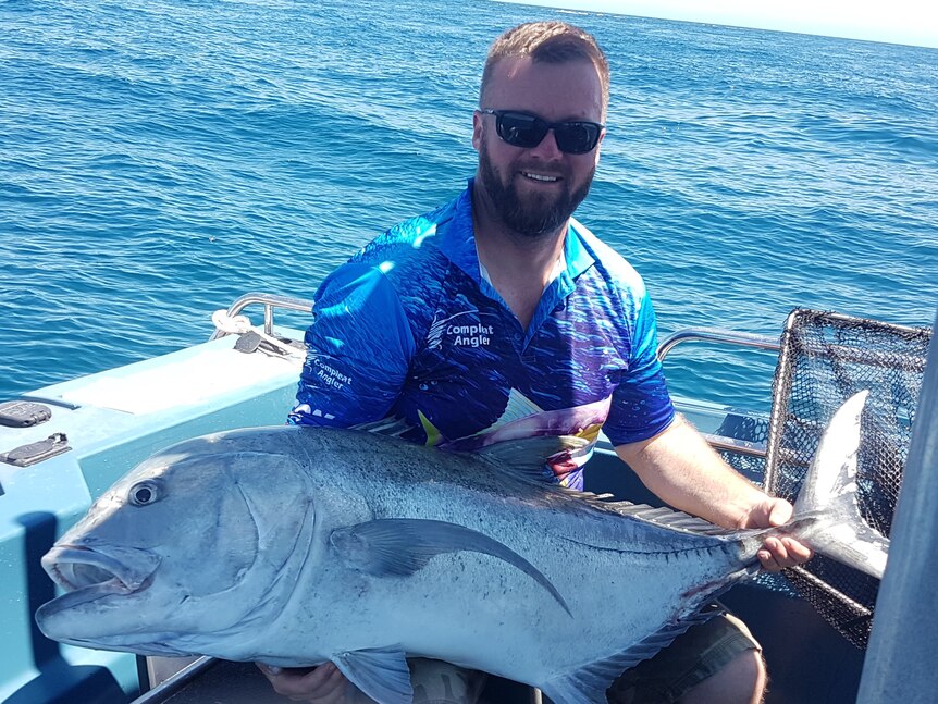 Man in blue shirt and sunglasses holding large fish on boat at sea.