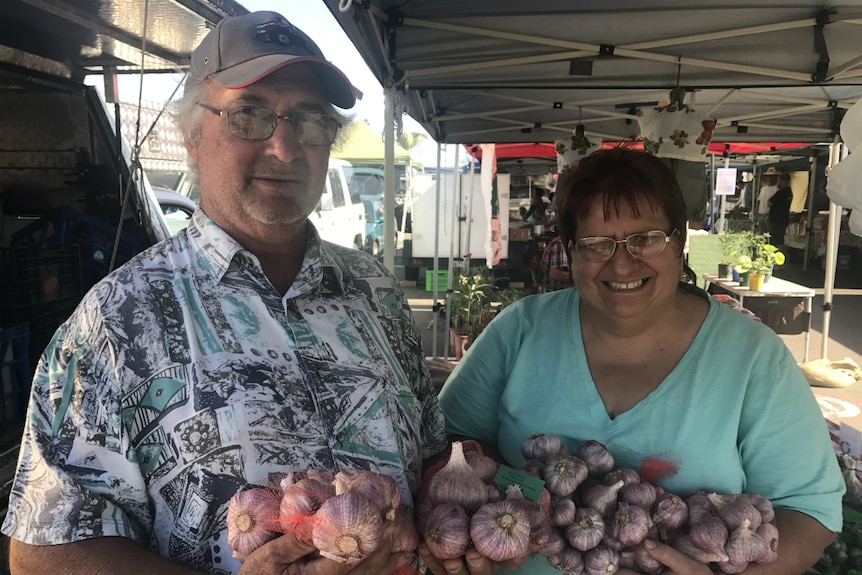 Leon and Lois Schroeder at their market stall with bags of garlic in their arms.