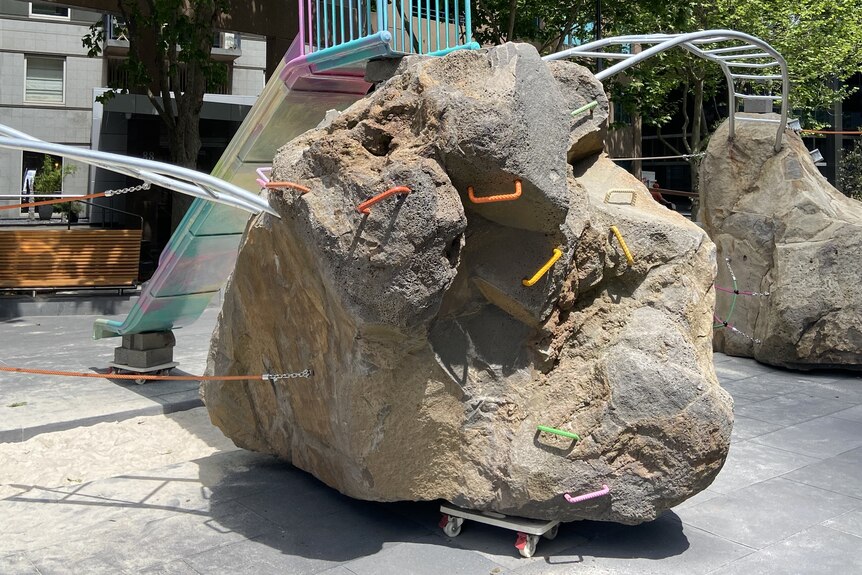 A boulder with hand grips bolted into it and a slide off the end