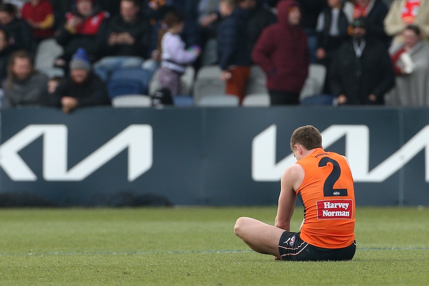 A GWS Giants AFL player sits alone on the field after his side lost to the Gold Coast Suns.