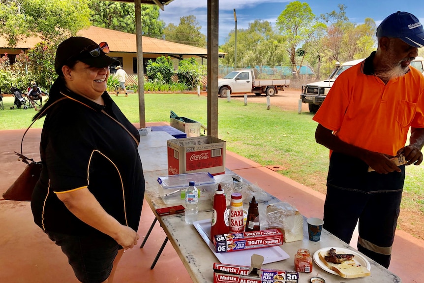 A woman stands behind a table full of breakfast food as a man lines up