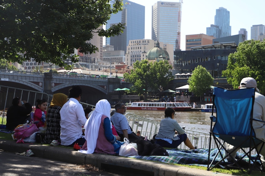 Multiple families sit on the banks of Melbourne's Yarra River