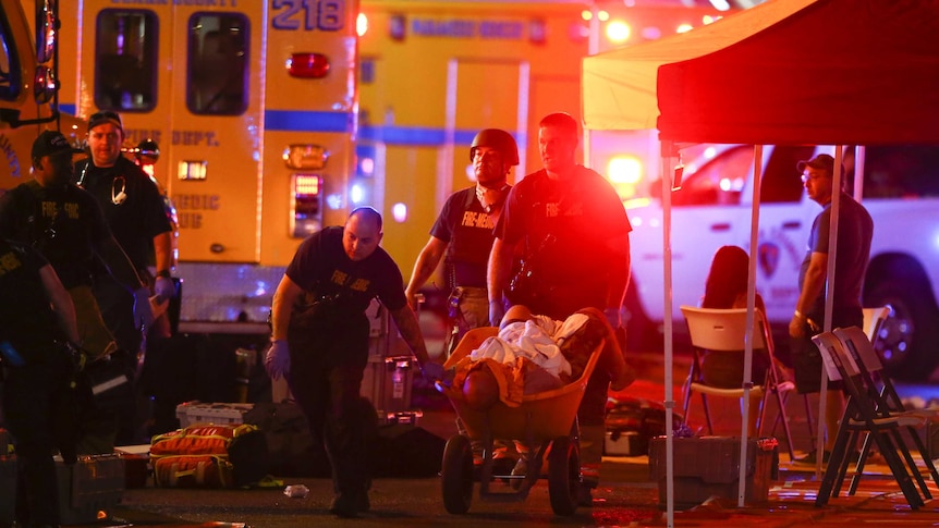 A wounded person is walked in on a wheelbarrow, ambulances attend to the scene