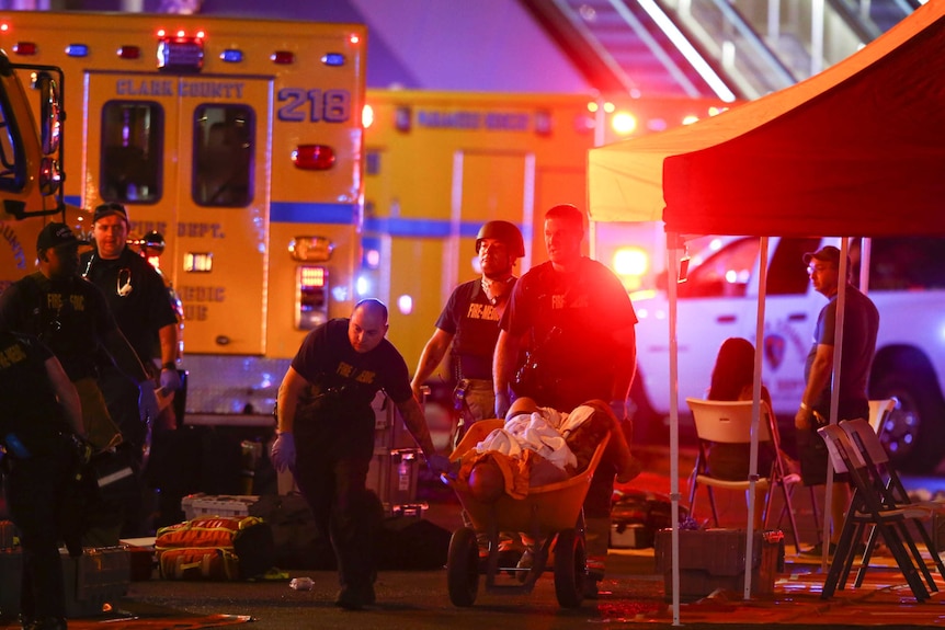 A wounded person is walked in on a wheelbarrow, ambulances attend to the scene