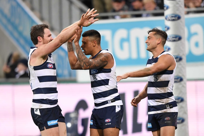 Three Geelong players celebrate after kicking a goal.