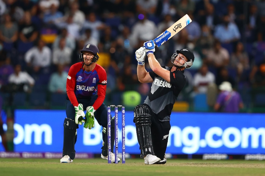 Jimmy Neesham holds his cricket bat above his head in both hands and looks up while down on one knee in front of the stumps.