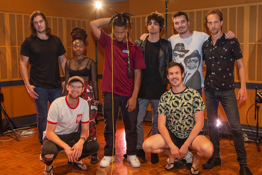 Group shot of band in studio with Curry holding microphone cord over head and Harvey and Stapleton in front row.