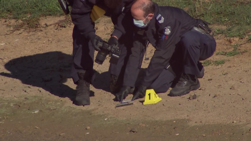 Two police officers standing by an item taking photos with an evidence marker next to it. 