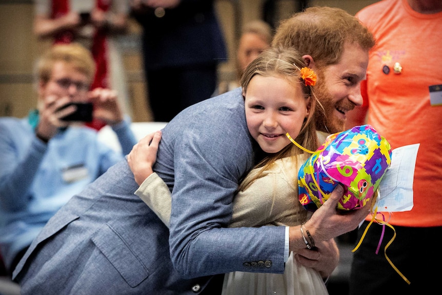 Prince Harry hugs a young girl while holding a brightly-wrapped present.