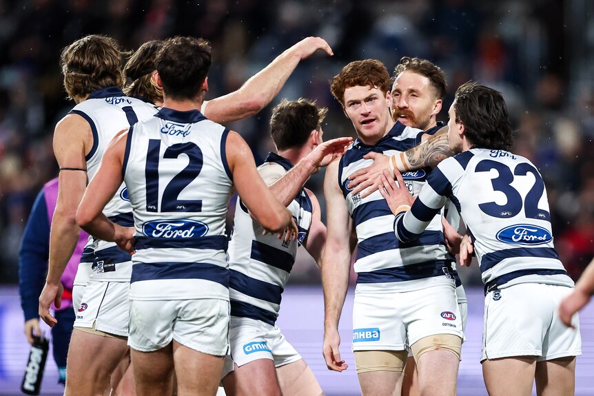 A Geelong forward stands silent in the rain as his teammates surround him after a goal.