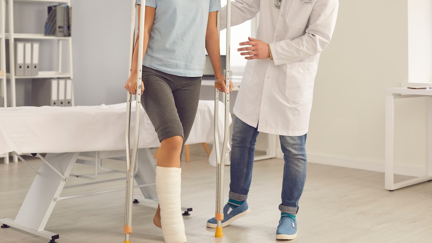 person on crutches with a leg cast taking a step with doctor supporting them