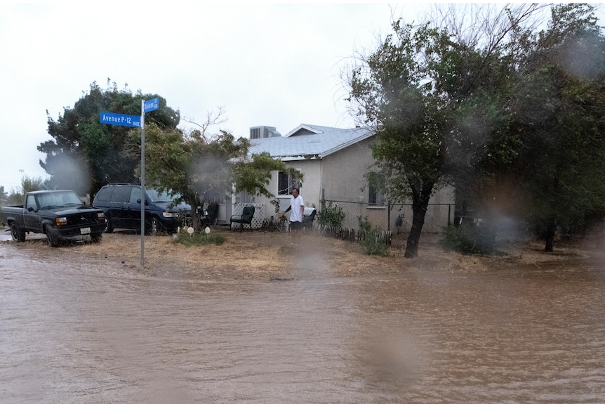 A man walks out of his house into muddy rain water.