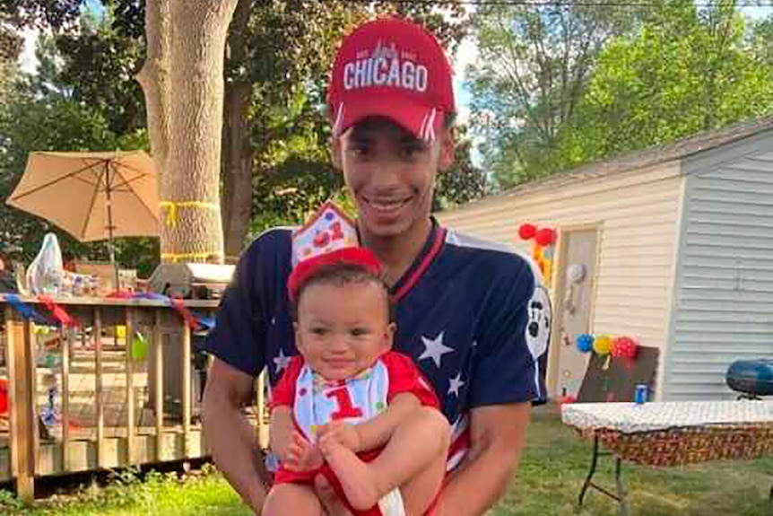 Man holds his 1-year-old son at a birthday party. 