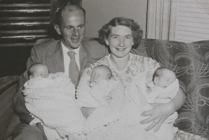 Black and white photo of a mother and father holding three babies.