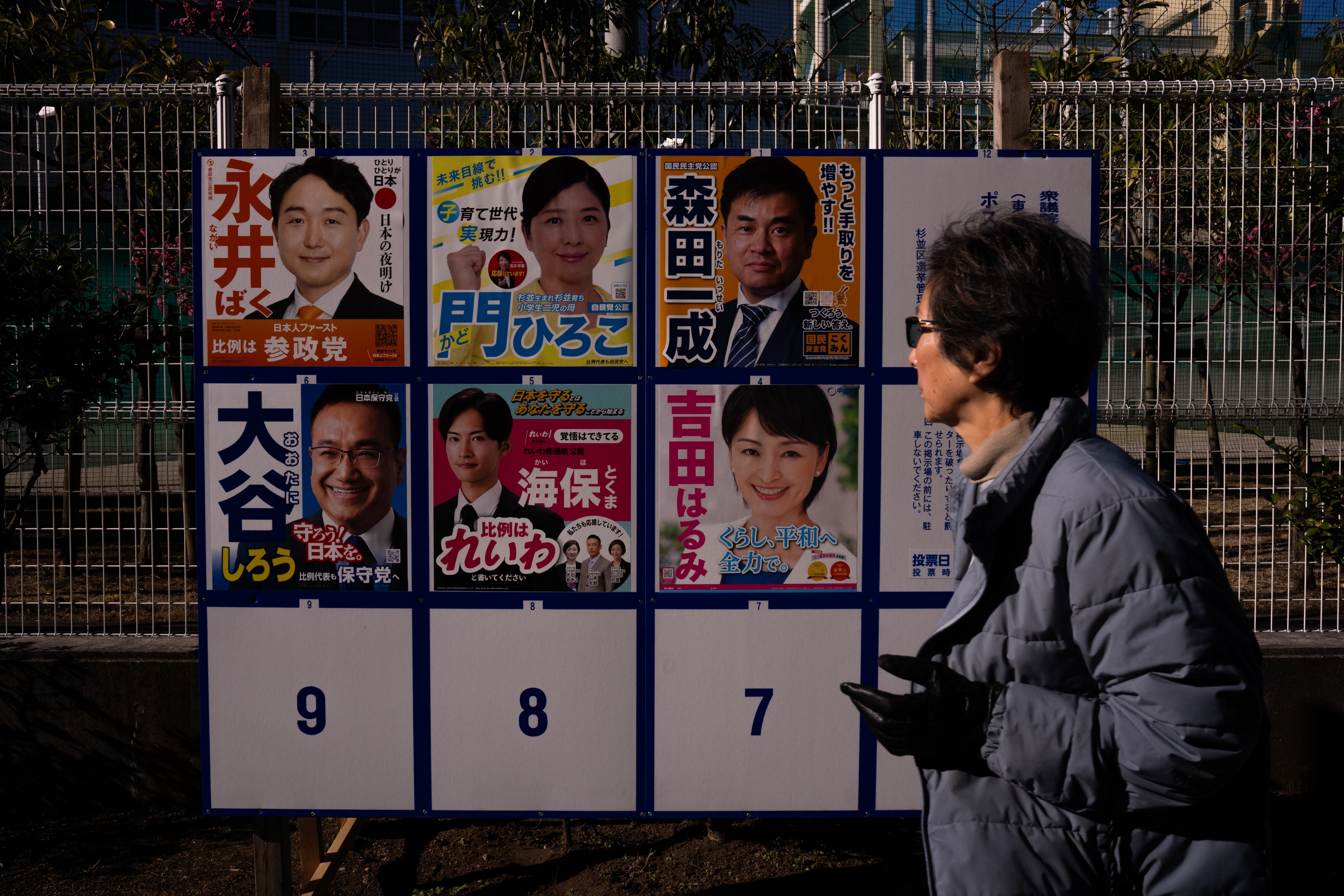 Una persona pasa junto a un tablero electoral en Tokio con carteles de candidatos
