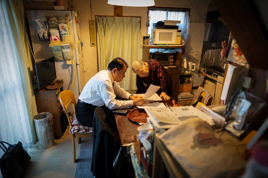 Detective Tsuchida shows a piece of paper to Setsuko in her kitchen