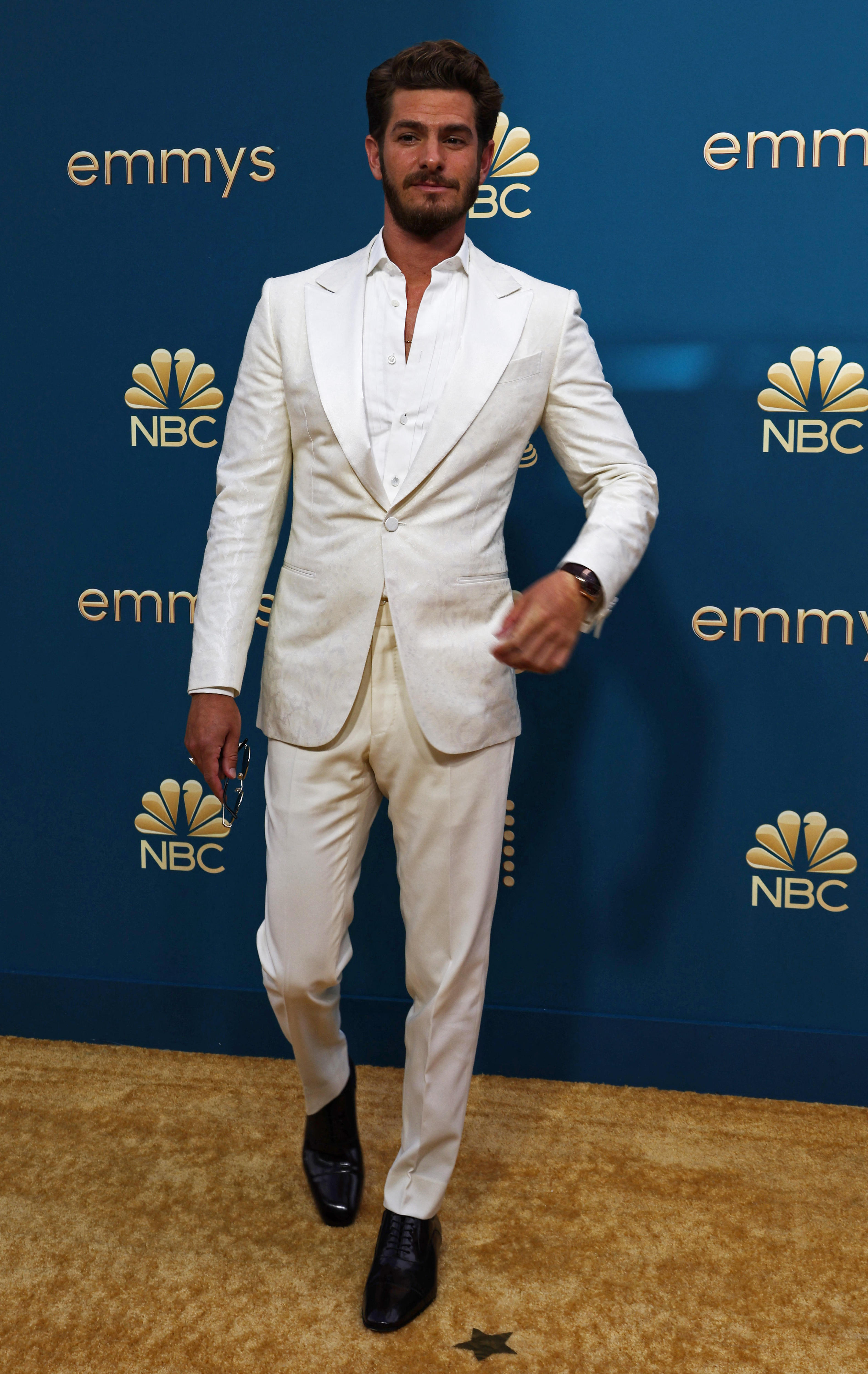 Andrew Garfield wearing an all-white suit, holding a pair of sunglasses