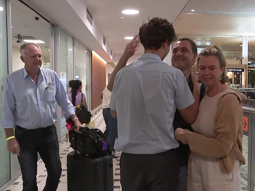 A family embraces at an airport in an emotional scene