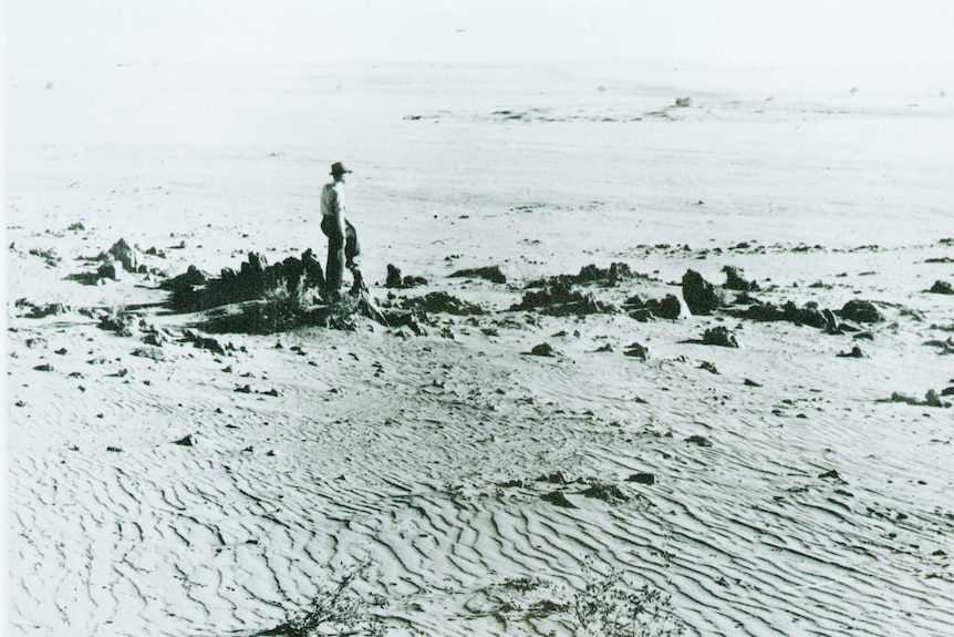 Black and white image of a man standing on a wind eroded expanse of land.