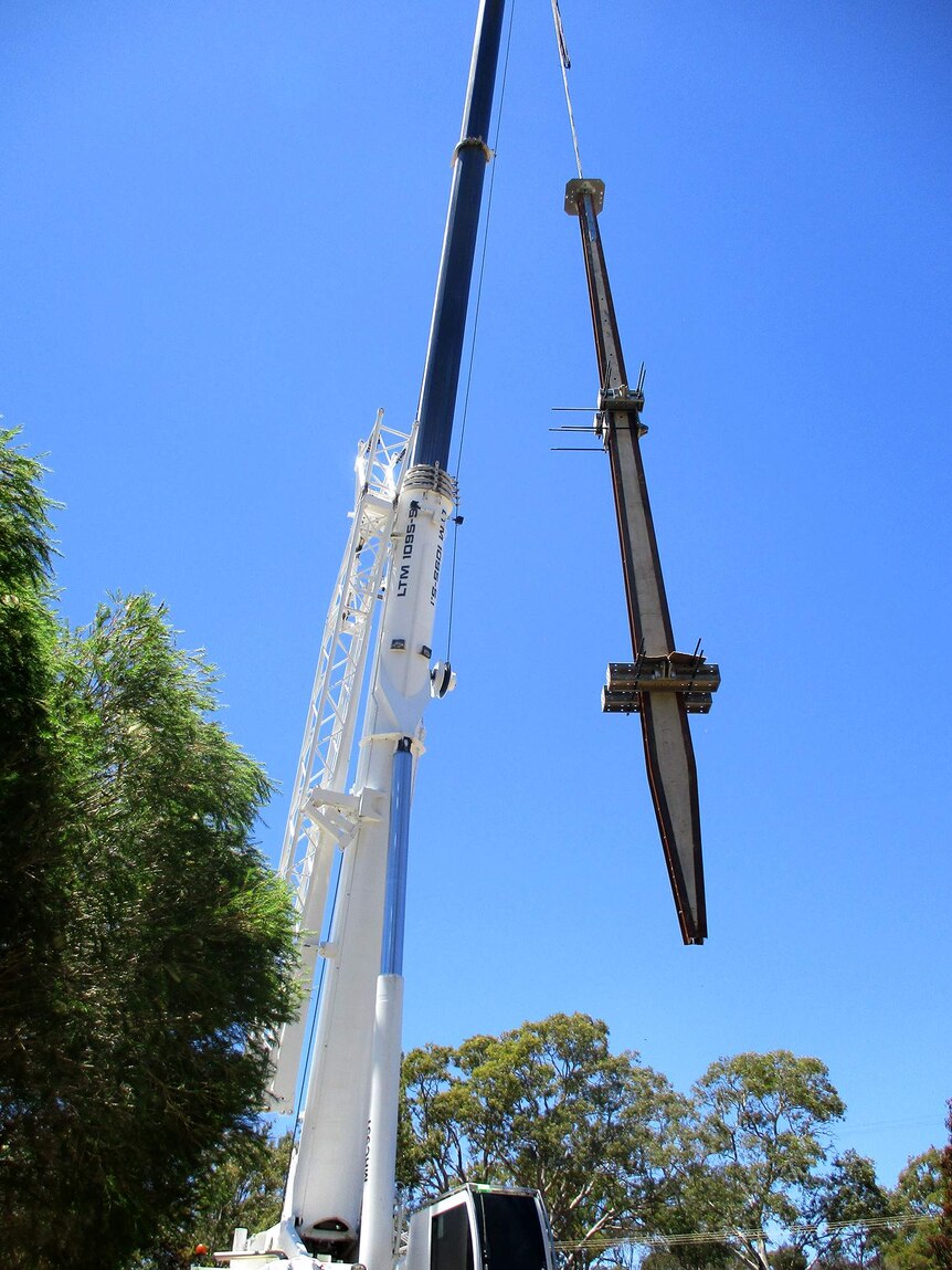 A crane holds a stobile pole in the air with blue skies in the background