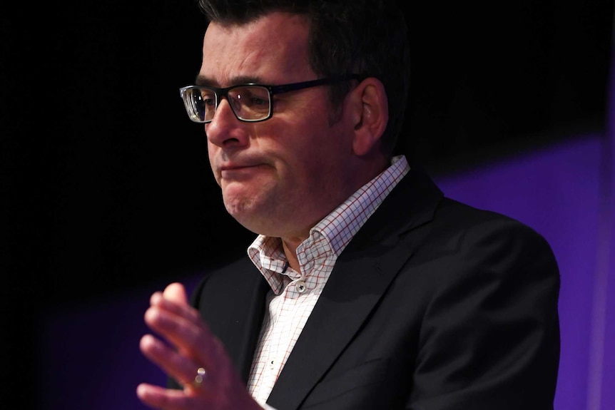 Victorian Premier Daniel Andrews makes a sad face behind a lectern in front of a media banner