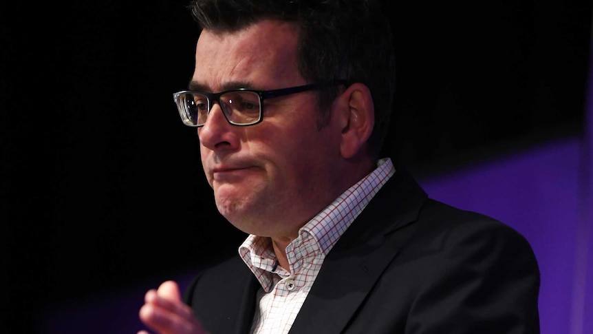 Victorian Premier Daniel Andrews makes a sad face behind a lectern in front of a media banner