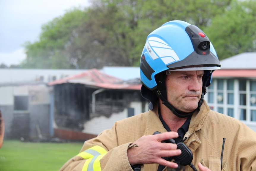 A man wearing fire gear in front of a fire damaged building