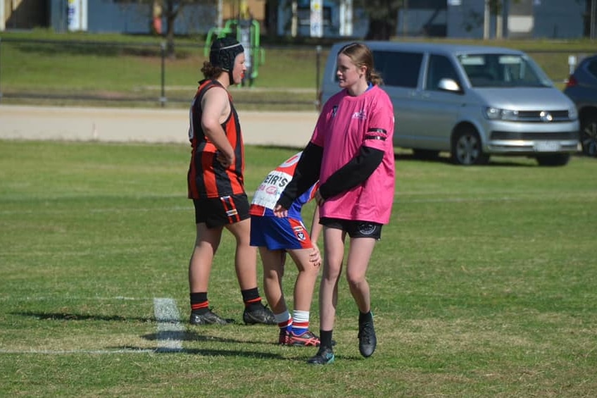 Aussie rules players and a runner on the field.