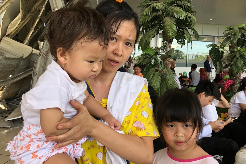 A mother and her two children wait outside at an airport