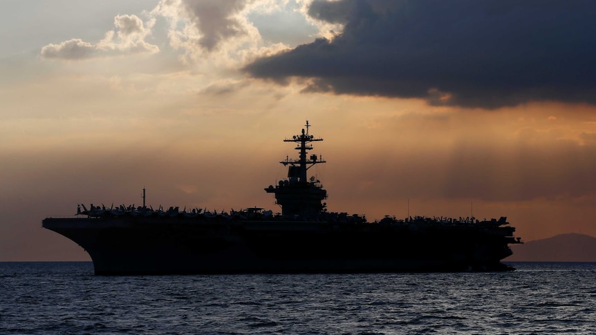The silhouette of the USS Theodore Roosevelt aircraft carrier against a dramatic sunset, near Manila.
