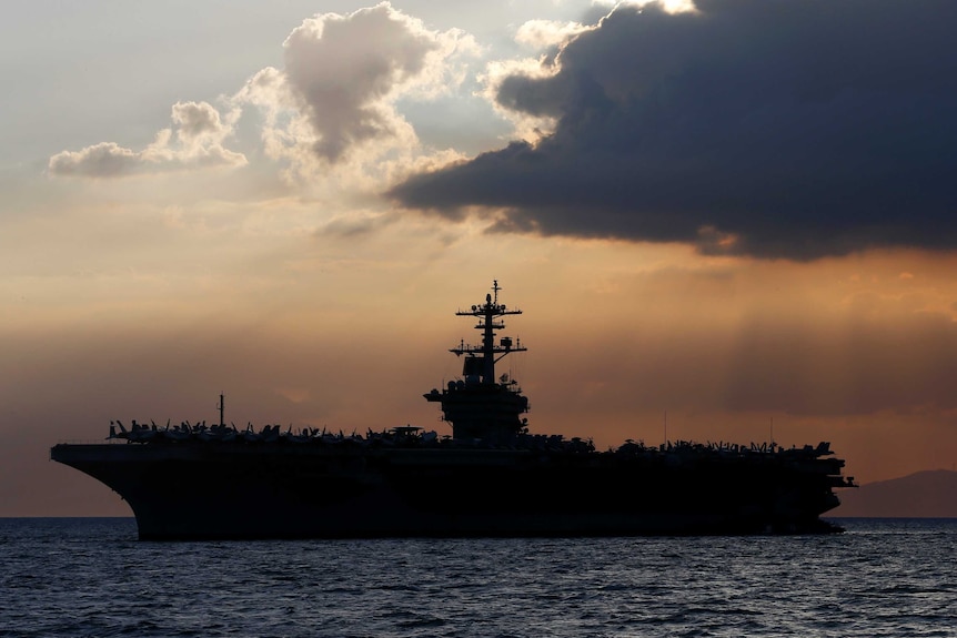 The silhouette of the USS Theodore Roosevelt aircraft carrier against a dramatic sunset, near Manila.