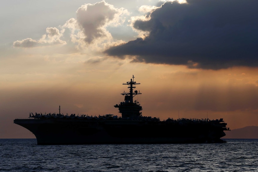 The US naval vessel USS Theodore Roosevelt in front of a sunset.