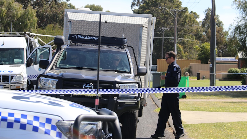 A forensics officer walks towards police cars 
