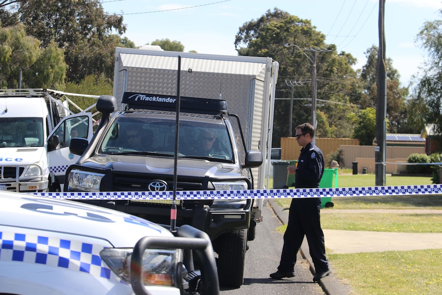 A forensics officer walks towards police cars 