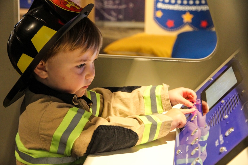A little boy, dressed up as a fireman, plays in an interactive museum