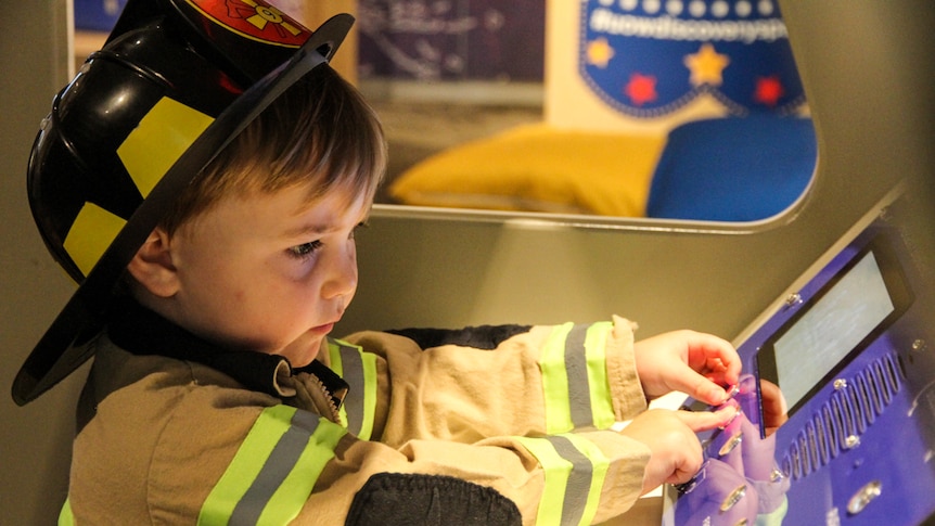 A little boy, dressed up as a fireman, plays in an interactive museum