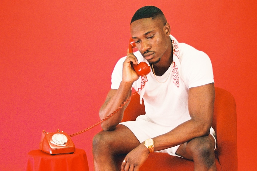 A man sits in a red chair in a red room holding a red telephone