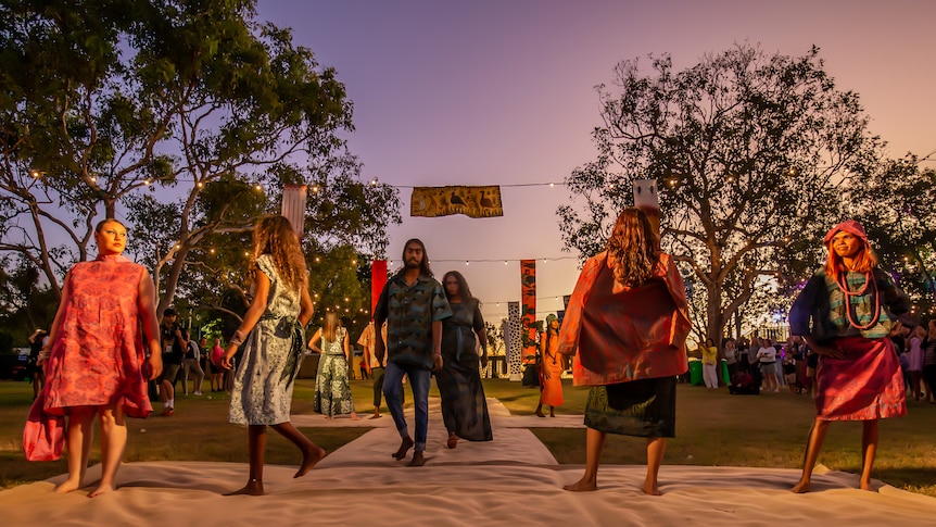 A group of models walk down a runway at an outdoor fashion show