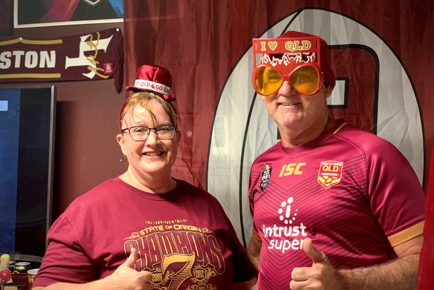 A couple dressed in Maroons regalia stand in their Queensland-themed den.