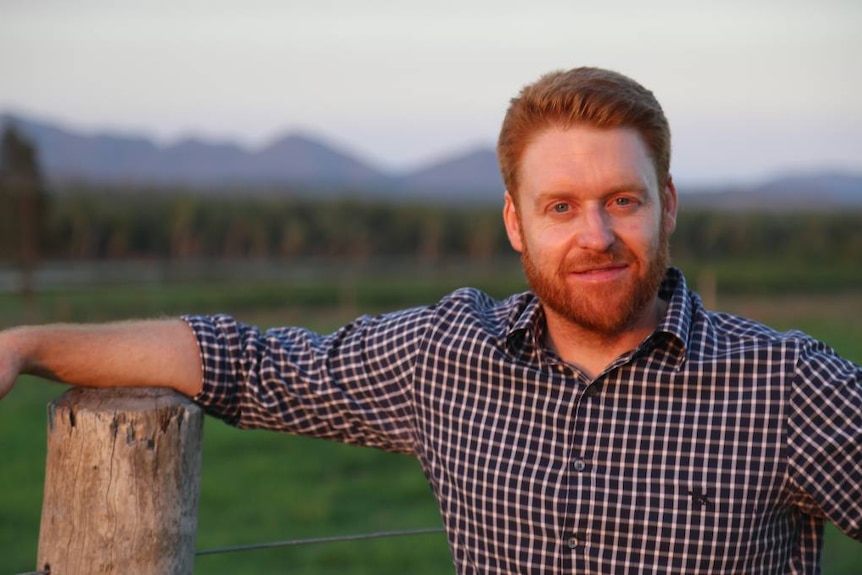 Mark Davie leans on a fence post and looks at the camera near a paddock in Queensland, date unknown.