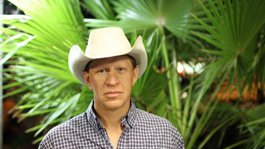 a man in a cowboy hat standing in front of palms