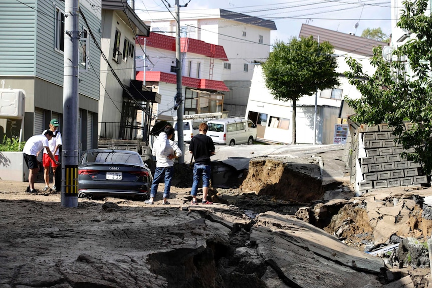 Residents look at a road that has collapsed and cracked in parts after an earthquake.