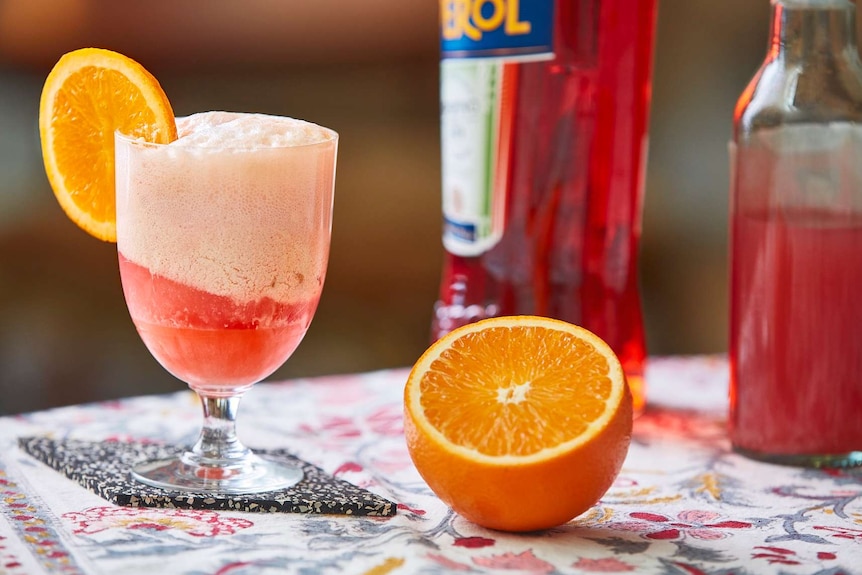 Aperol float in a glass next to an orange to depict a collection of low-alcohol cocktail recipes.