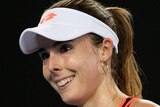 Alize Cornet, wearing an athletic outfit and visor, smiles as she walks on a tennis court.