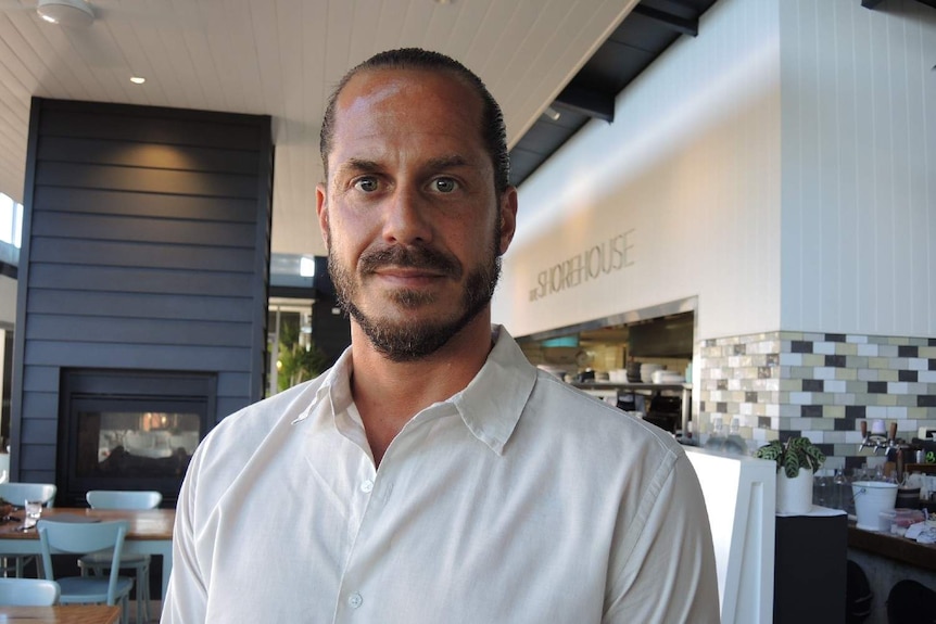 George wearing a white shirt, in the centre of a modern restaurant with a bright  interior.