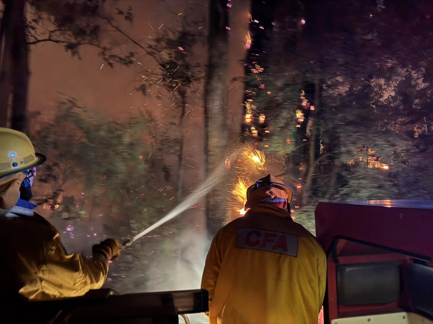 Los bomberos apuntan con su manguera a un incendio forestal nocturno.