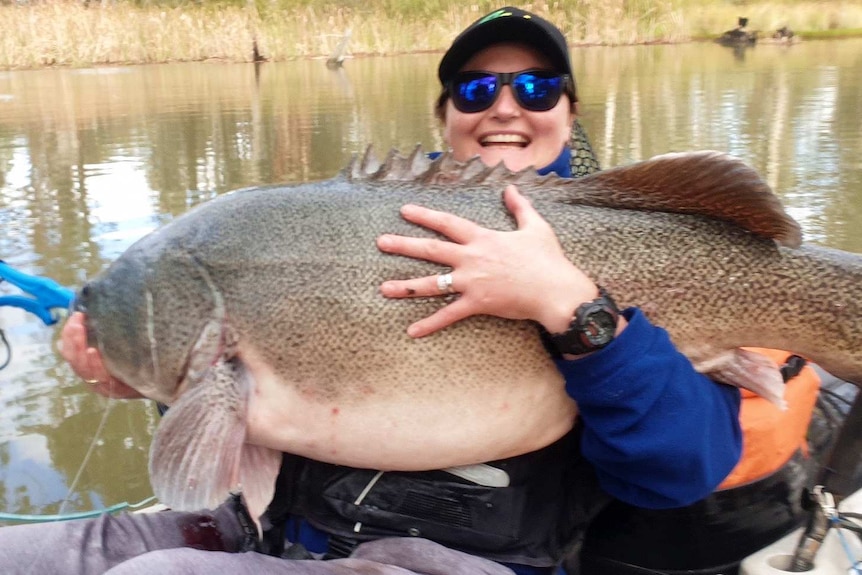 A lady smiles at the camera as she holds a giant fish