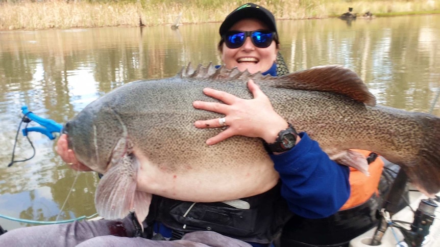A lady smiles at the camera as she holds a giant fish.